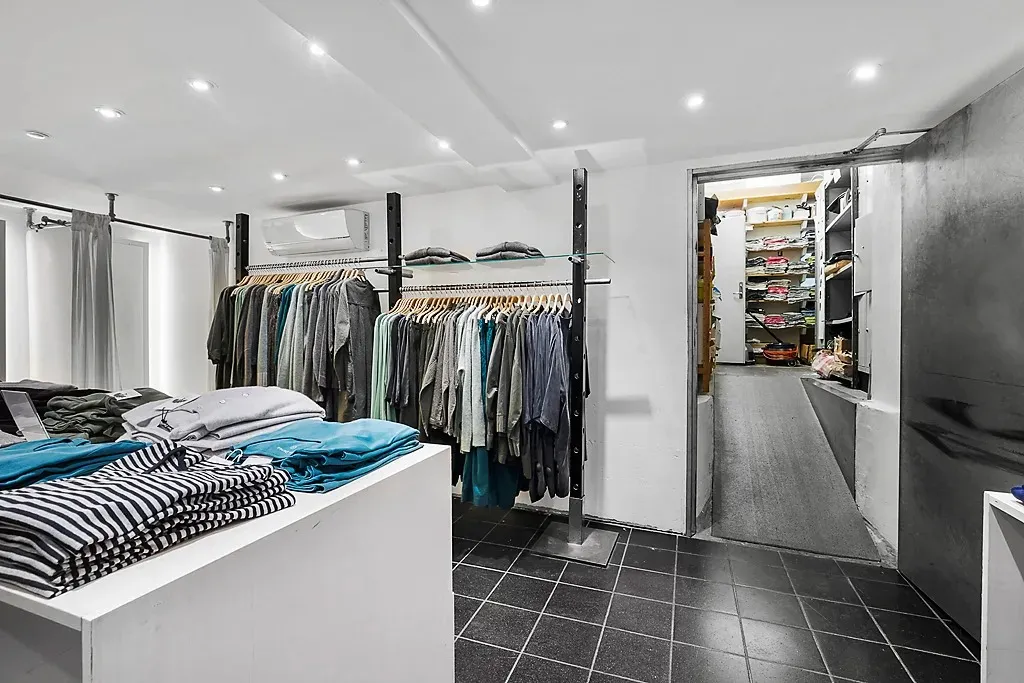 En ren og velorganiseret tøjbutik med tøj på hylder og tøjstativerne og tøj på bordet og et lukket skab til højre