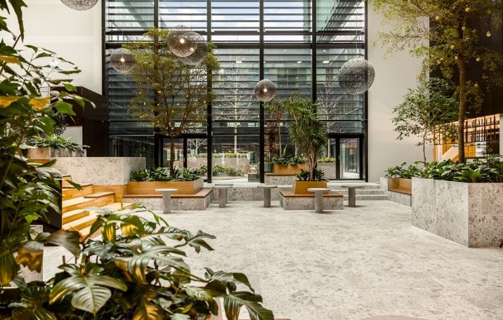 Smuk lobby med grønne planter, lyse gulve, lyse træbænke og store runde lysekroner i loftet