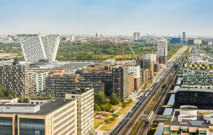 København med mange højhuse og tætte bygninger, en stor vej med togspor og biler, og træer i baggrunden