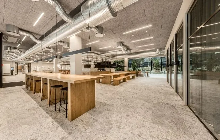 Et stort kontor med træborde og stolpe, samt gulv-til-loft-vinduer med byudsigt, en stor hall med plantager og et hvidt loft