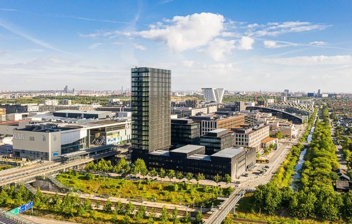 Bygninger med gulv-til-loft-vinduer og moderne arkitektur på et større byområde med grønne områder og vegetation langs