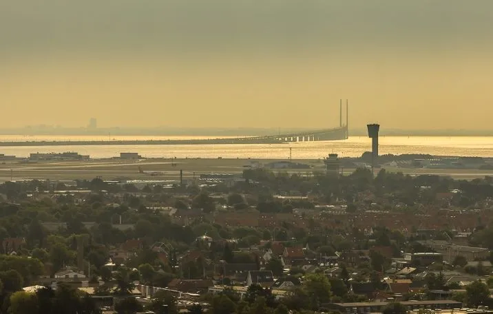 Luftfoto over Københavns Lufthavn med lufthavnsbygning, tårn, bro, og bygninger med røde tag. Haver og grønne områder, og
