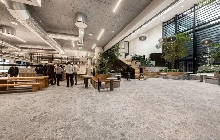 Kontorlokaler med moderne interiør, store vinduer, grønne planter og en elegant, træfarvet spisestue