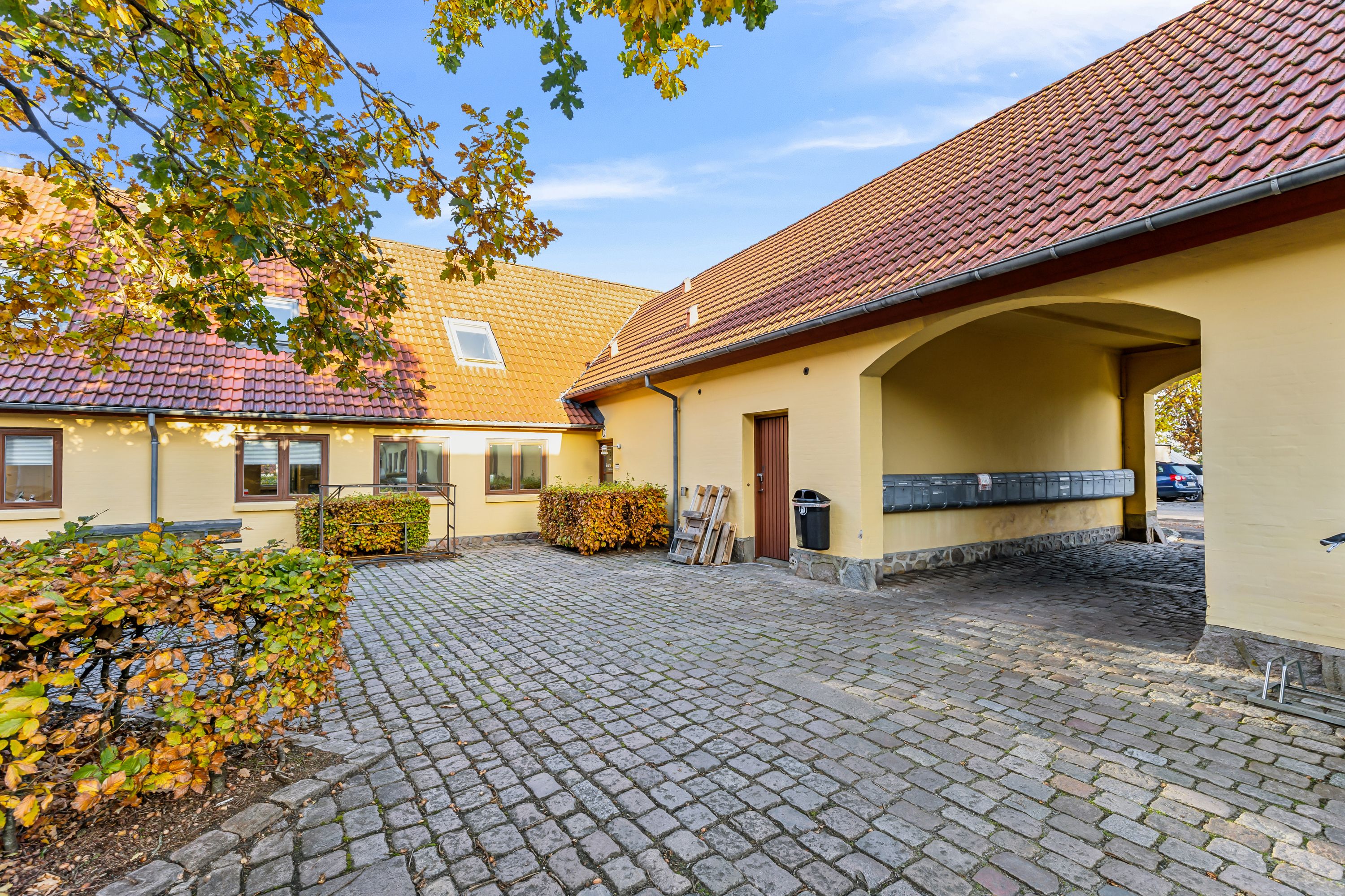 På et lyst og solrigt efterårsdag er der et gammelt hus med røde tagtegel og gulmalet vægge. Det er en charmerende