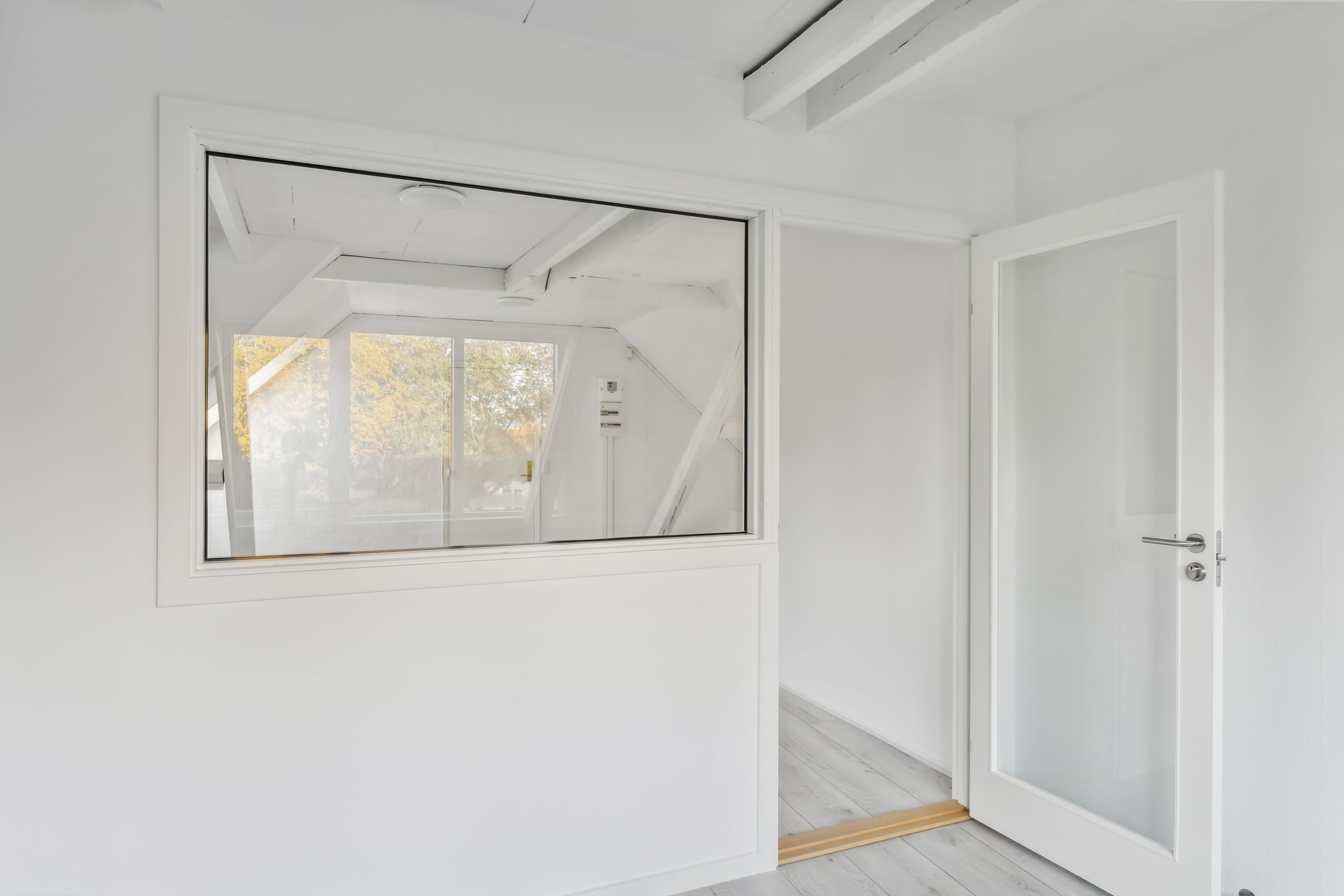 En lys, hvidt malet rum med et vindue og en dør, der vender mod et indre loft og et højt gulv