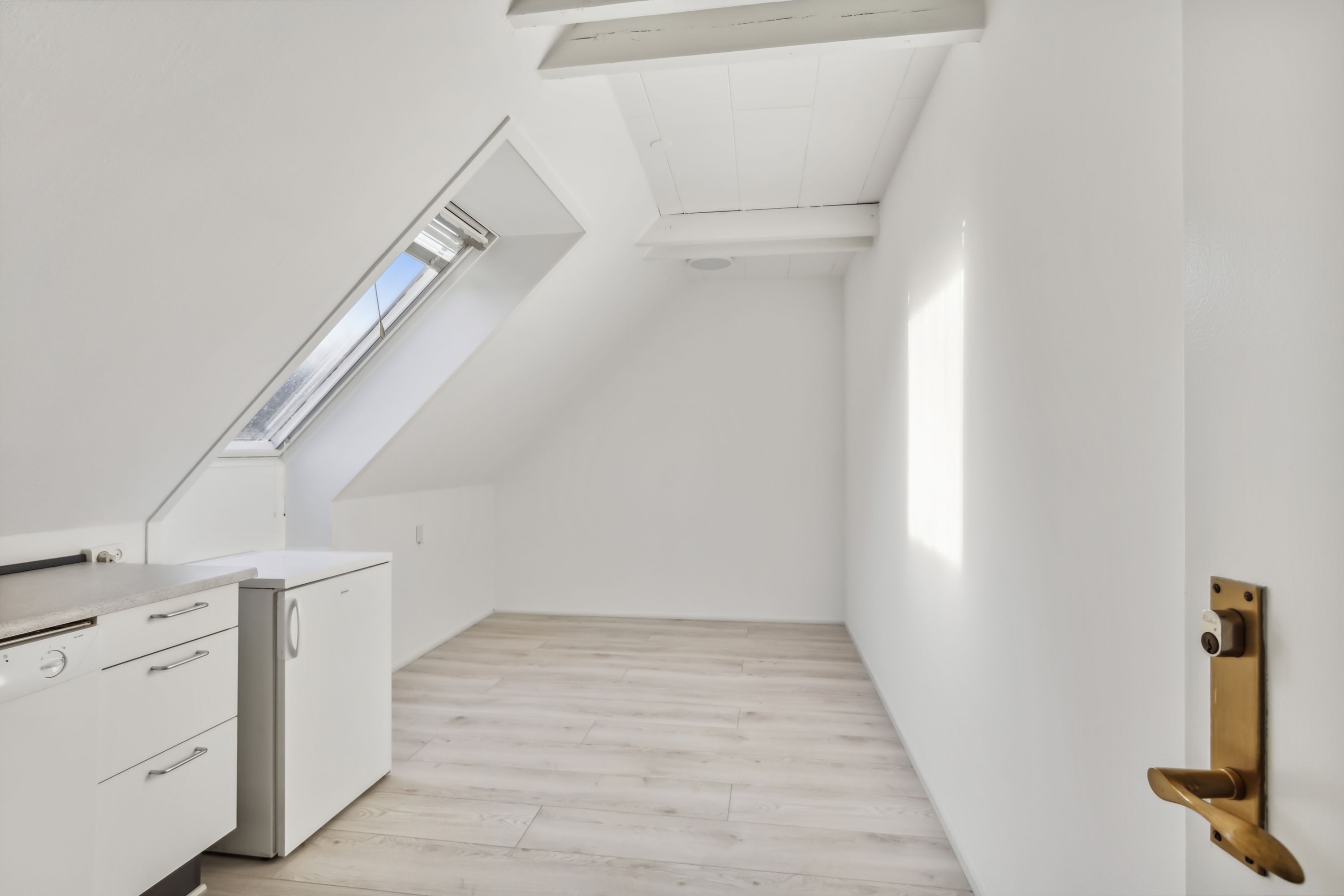 Hvidt køkken med højloft og lysevinduer, hvid gulv og køleskab, håndtag og tærskel i messing.