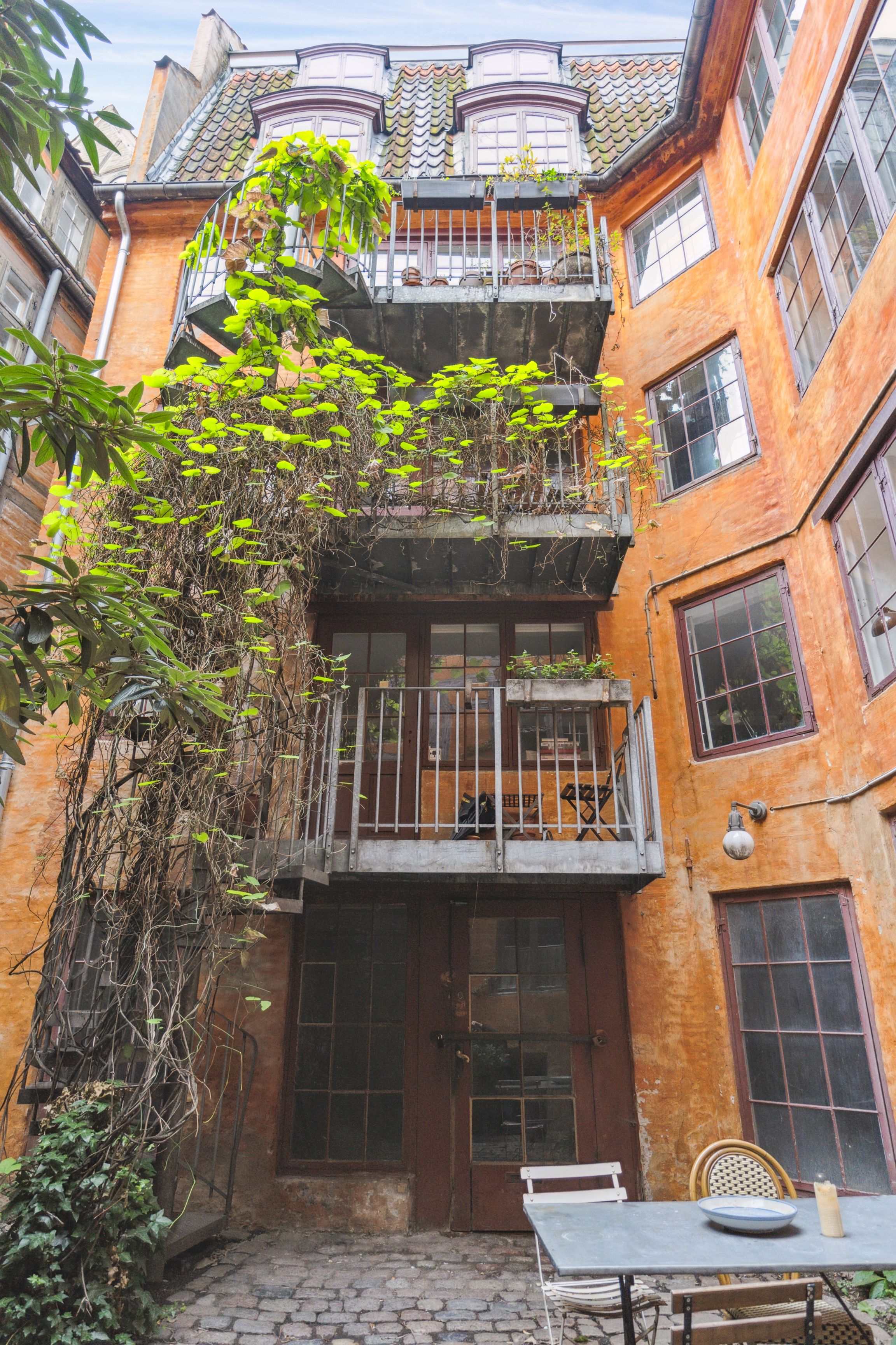 En nyrenoveret orange bygning med terrasser og plantager og et ståbord med tallerken og stearinlys på