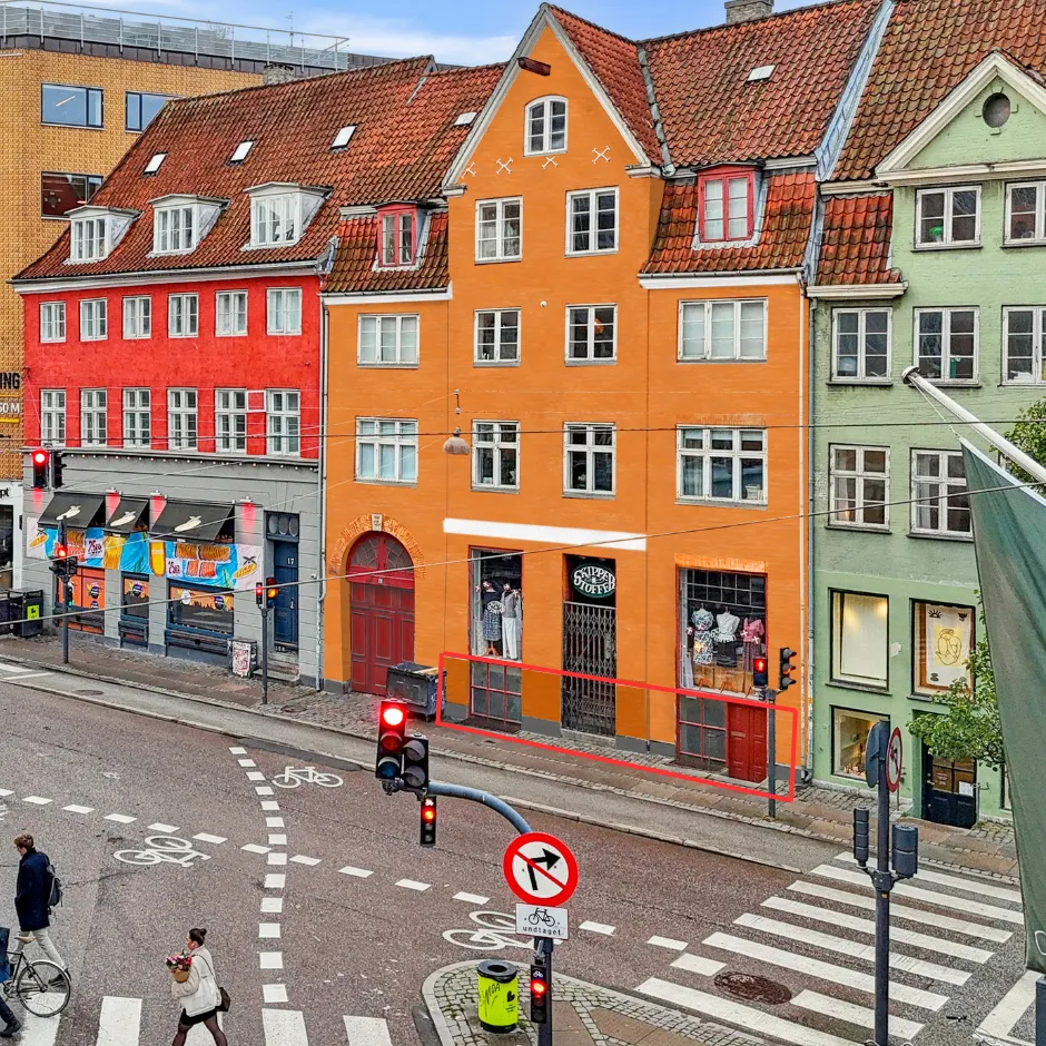 En stærkt renoveret ejendom i København med røde, gule og grønne facader og røde tag. På gaden er der gågade med kryds og