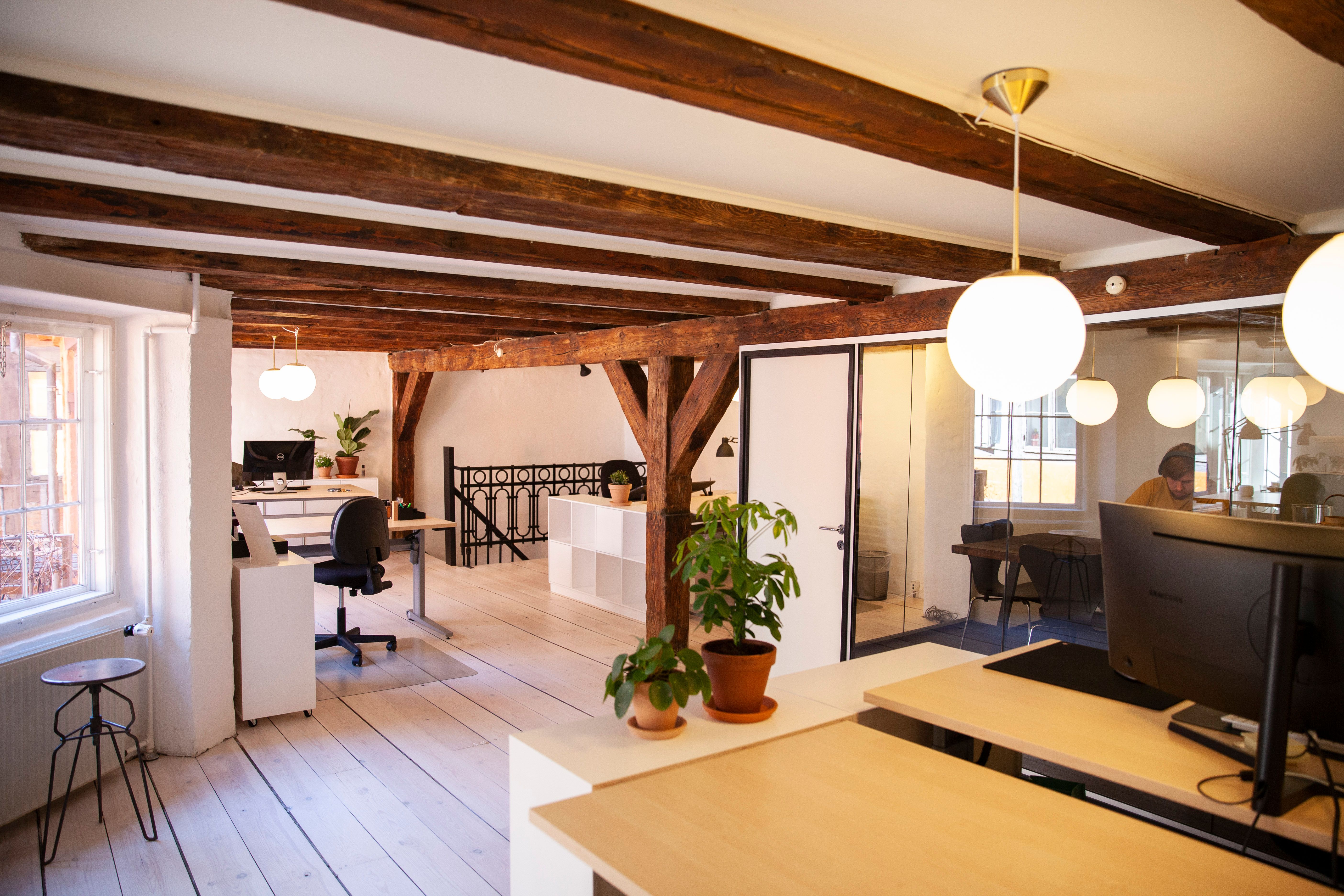 Kontor med åbent plan og moderne møbler, to plantepottter, en stol og en computer med skærm, hængelampe, lysekroner, en