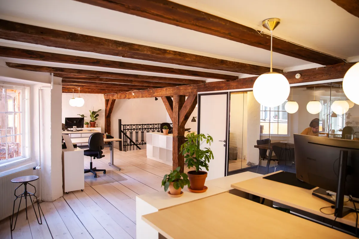 Kontor med åbent plan og moderne møbler, to plantepottter, en stol og en computer med skærm, hængelampe, lysekroner, en