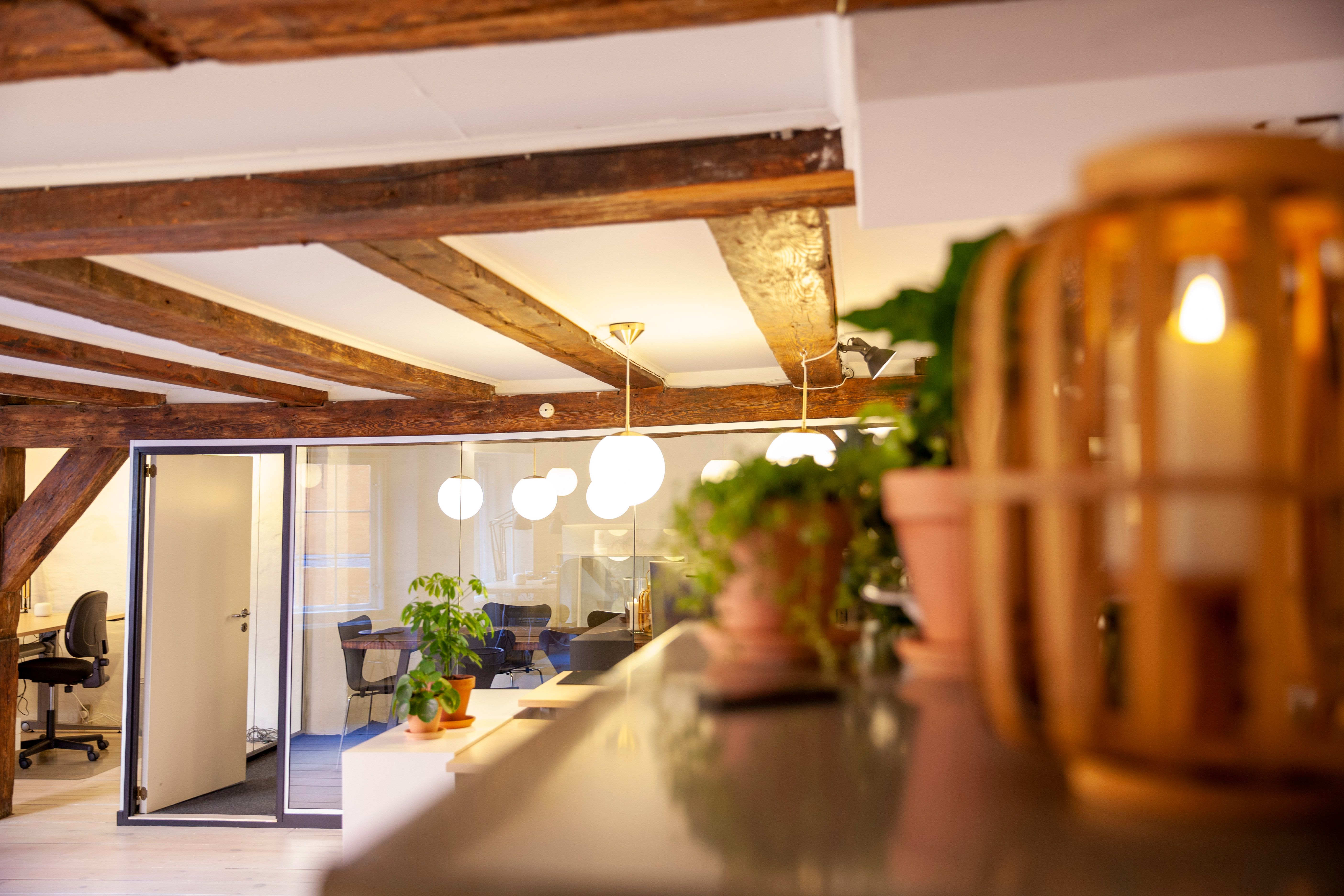 Kontor med træloft, lysekroner, grønne planter og stol i baggrunden og lysegult lys på loftet