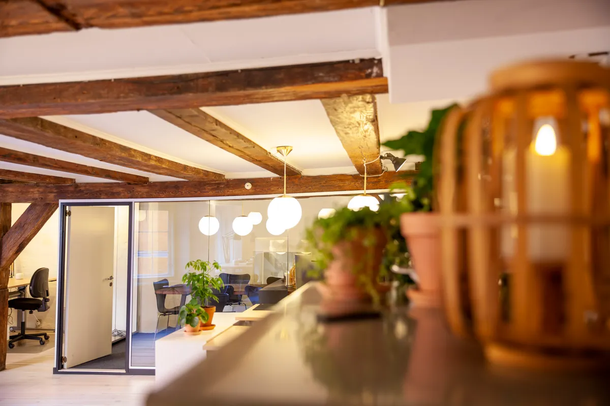 Kontor med træloft, lysekroner, grønne planter og stol i baggrunden og lysegult lys på loftet