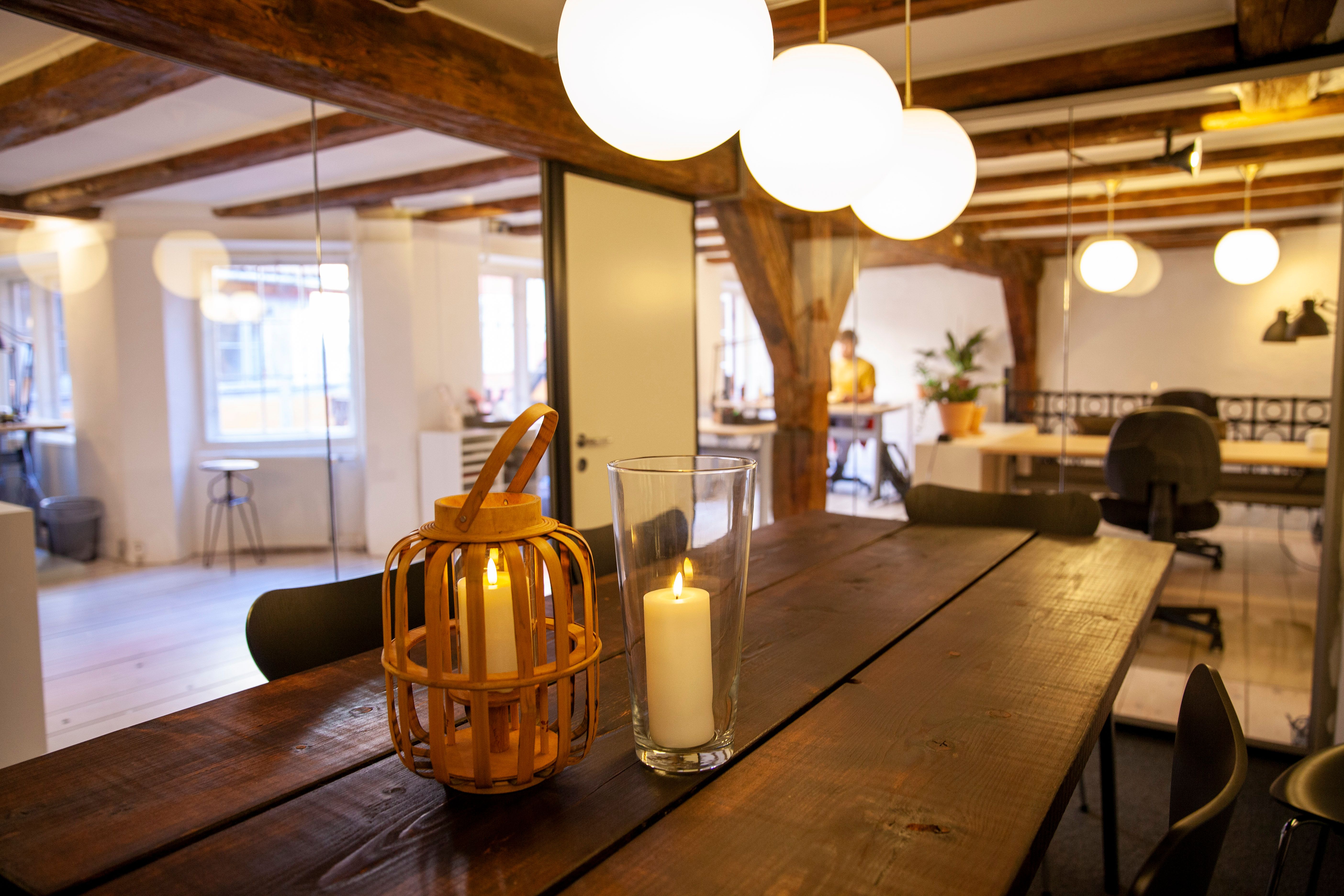 En køkkenbord med to stearinlys i glasset og en lanterne samt flere stole i køkkenområdet