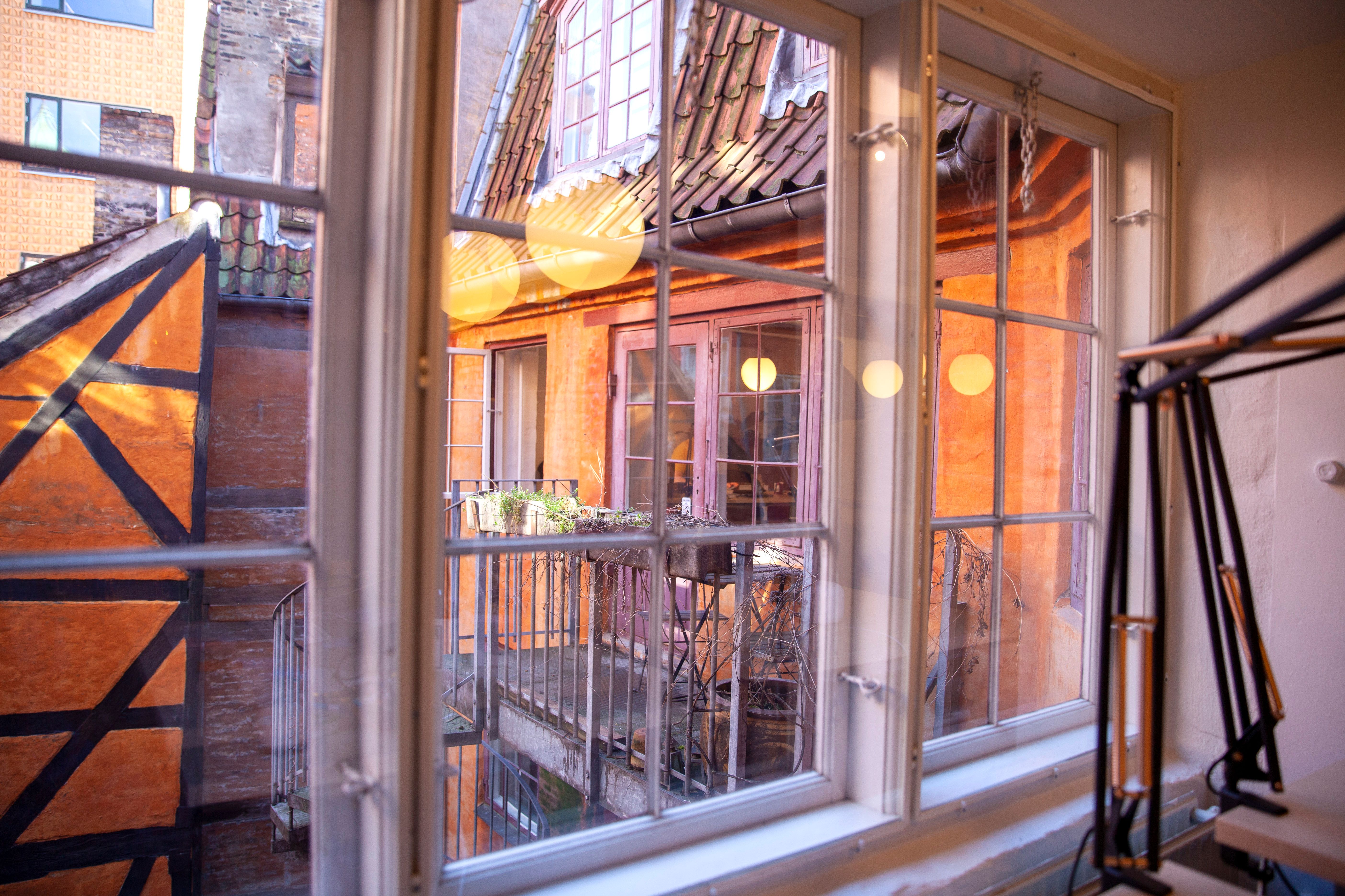 Vindue med udsigt til bygning med terrasse og lysereflekser, som skaber varme og hyggelige atmosfærer, og udendørs møbler
