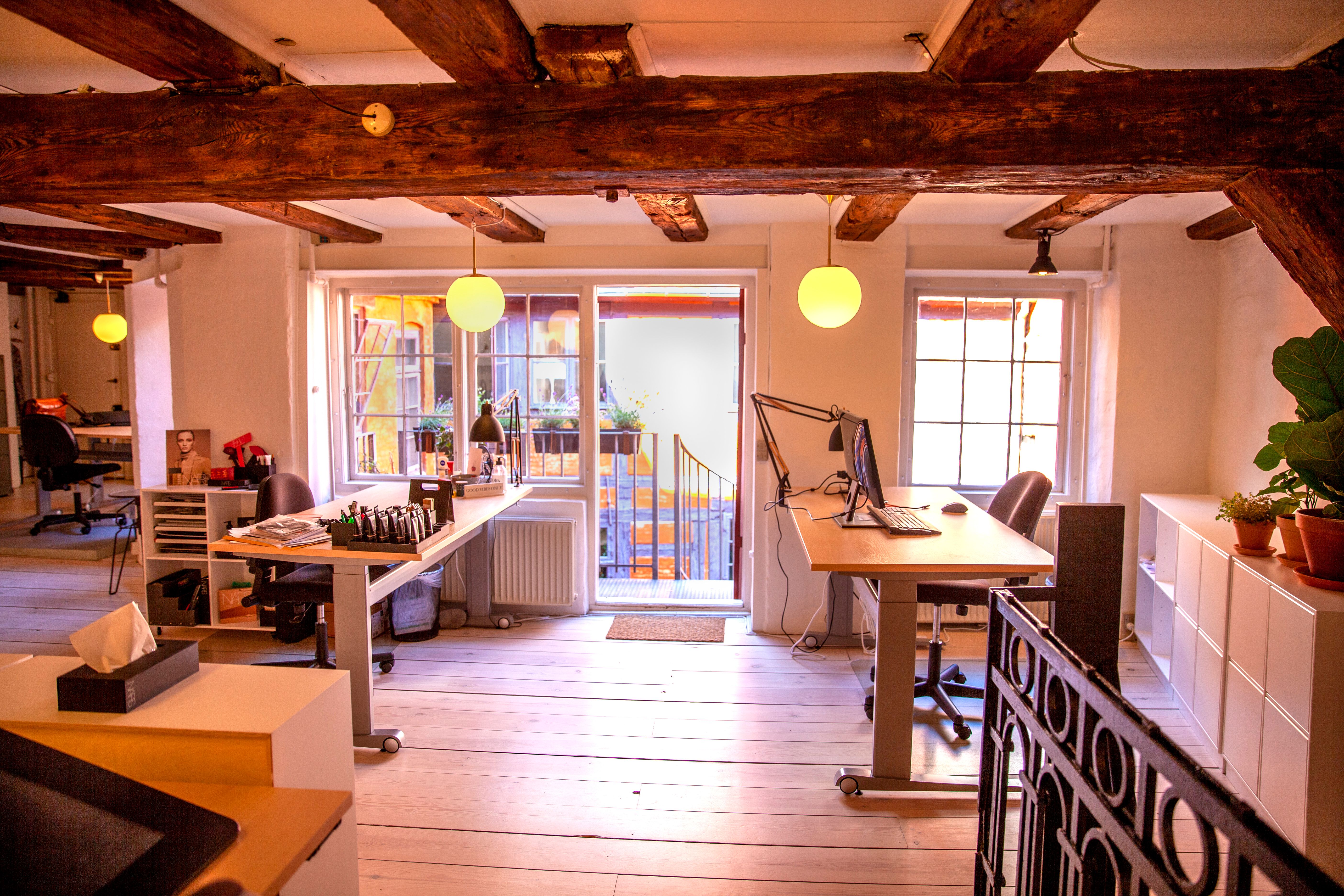 Kontor med højloft, hvor to skriveborde og kontormøbler er placeret under lyse lysekroner. Højre side har en computer og en