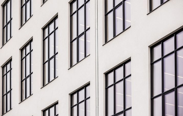 Moderne kontorbygning med store, rektangulære glasruder og sorte rammer. Bygningen er sandblæstet og hvidmalet.