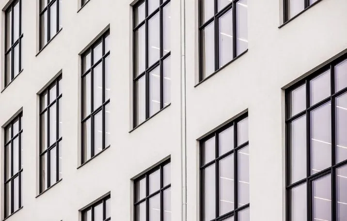 Moderne kontorbygning med store, rektangulære glasruder og sorte rammer. Bygningen er sandblæstet og hvidmalet.