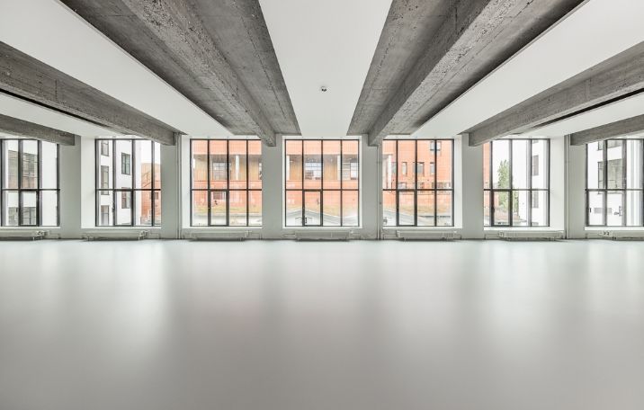 Et stort, tomt kontorrum med højt loft og sandblæstede søjler og store glasruder