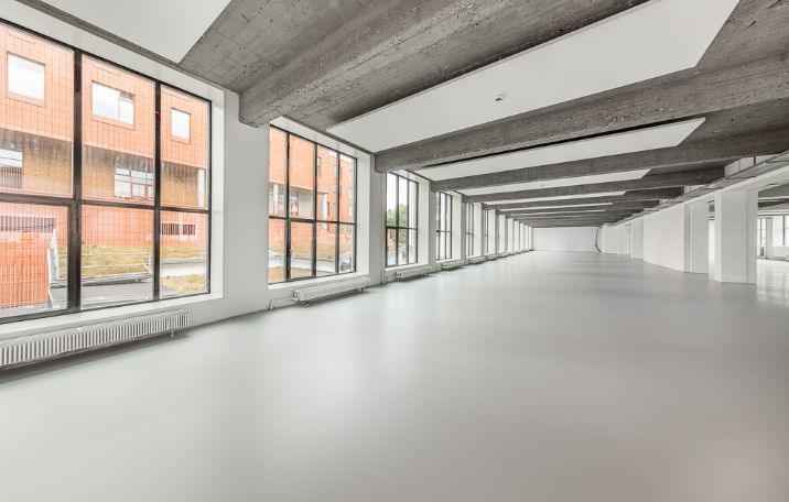 Sandblæste søjler og store glasvægge med sorte sprosse. Moderne kontor med åben gulvplan. Store vinduer med udsigt til