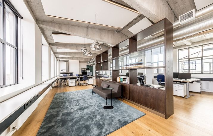 Kontor med rå fabrikstil og sandblæste søjler, glasvægge og lofter med lysearme, der giver mængder naturlys