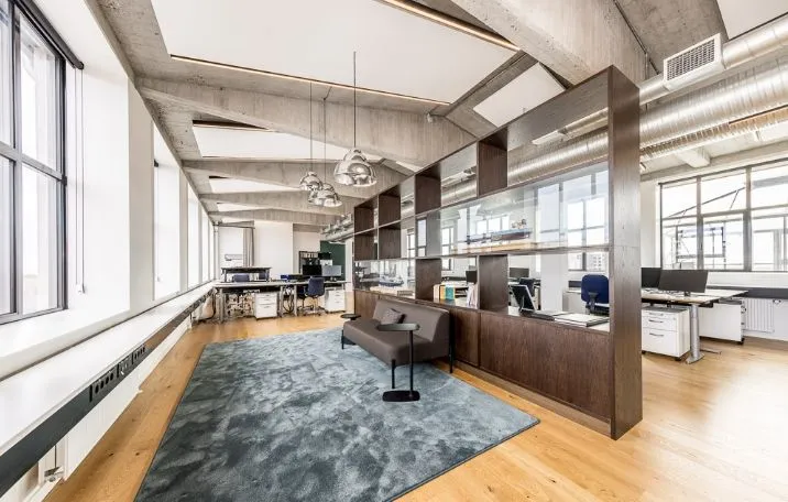 Kontor med rå fabrikstil og sandblæste søjler, glasvægge og lofter med lysearme, der giver mængder naturlys