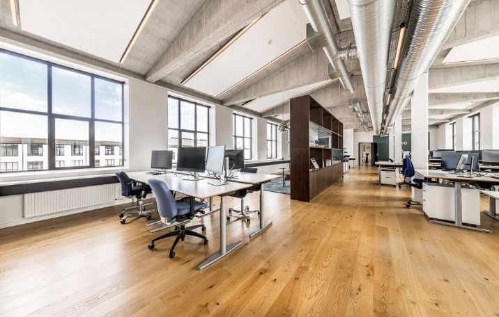 Kontor med store vinduer og trægulv, moderne design med højt loft og lyse søjler