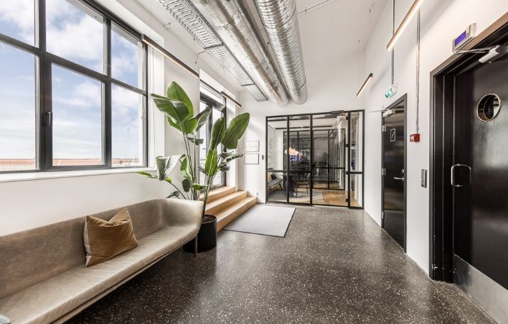 En moderne, rå fabriksstilskontor med sandblæste søjler og glasvægge i sorte sprosser