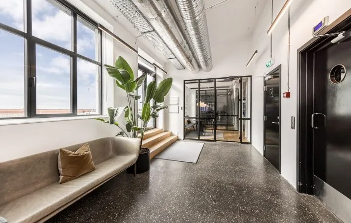 En moderne, rå fabriksstilskontor med sandblæste søjler og glasvægge i sorte sprosser