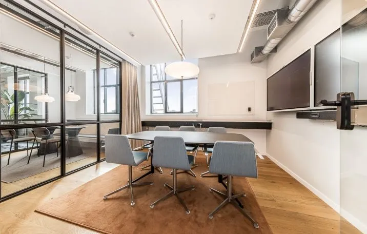 Kontor med glasvægge og søjler i rå fabrikstil, moderne møbler og tv-skærme