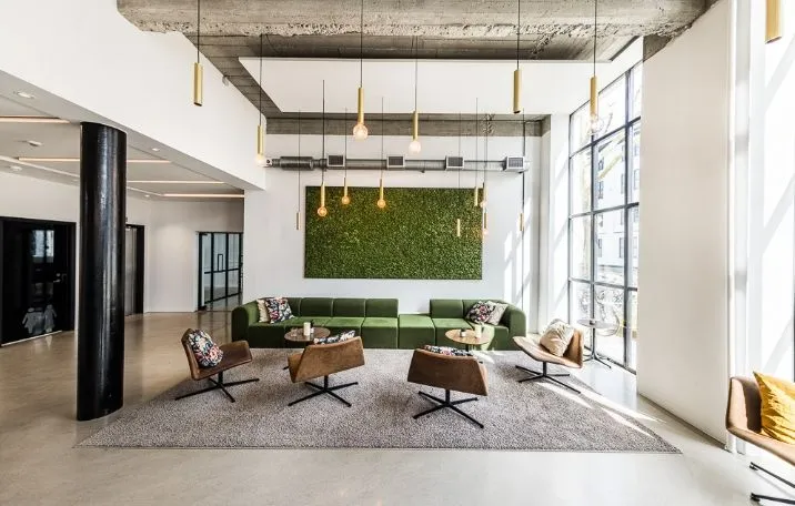 Moderne kontor med sofaer og stole omkring runde bord, lyskroner og grøn væg, søjler og glasvinduer