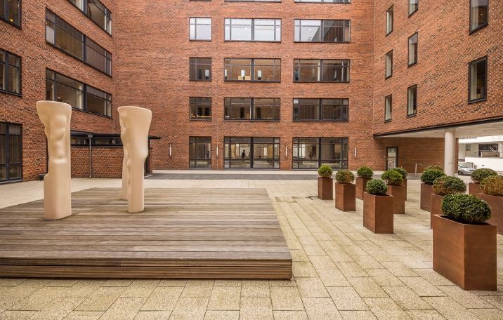 Kontorgård med terrasse og kunstværker i lysegult. Moderne kontorlokaler med store vinduer og trægulve