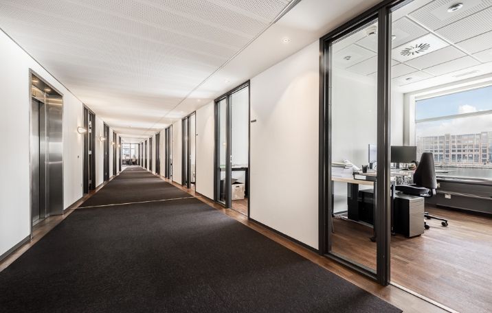 Moderne, lyse kontorlokaler med højloft og trægulv, glasdøre og træbord med computer og telefon