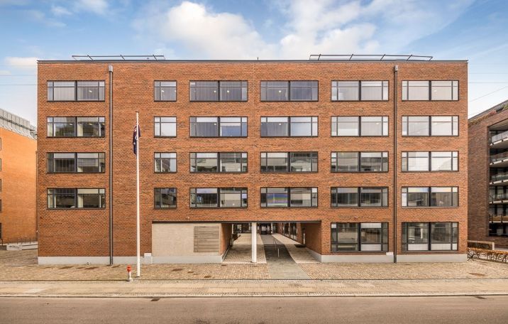 Kontorlokaler i moderne bygning med mange vinduer og en lyseblå himmel med skyer i baggrunden