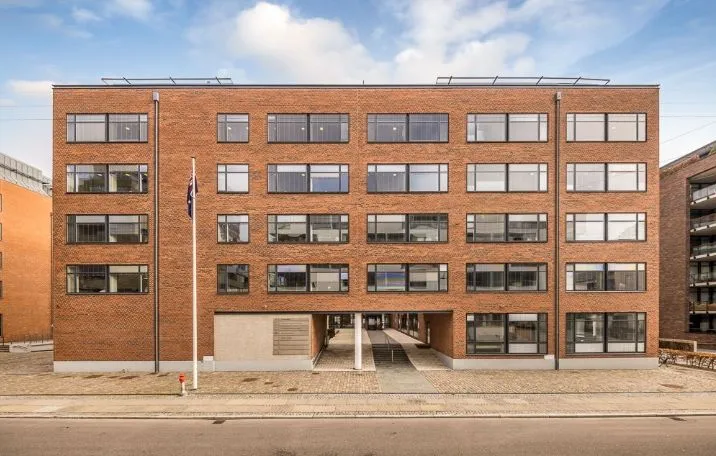 Kontorlokaler i moderne bygning med mange vinduer og en lyseblå himmel med skyer i baggrunden