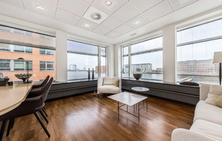 Kontorlokaler med udsigt til vandet, højloft, moderne møbler og en hvid sofa med pude