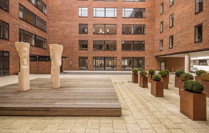 Kontorlokaler med skulpturer, plantekasser og glasvinduer i kvarteret. Moderne og rummelige lokaler med trægulv og terrasse