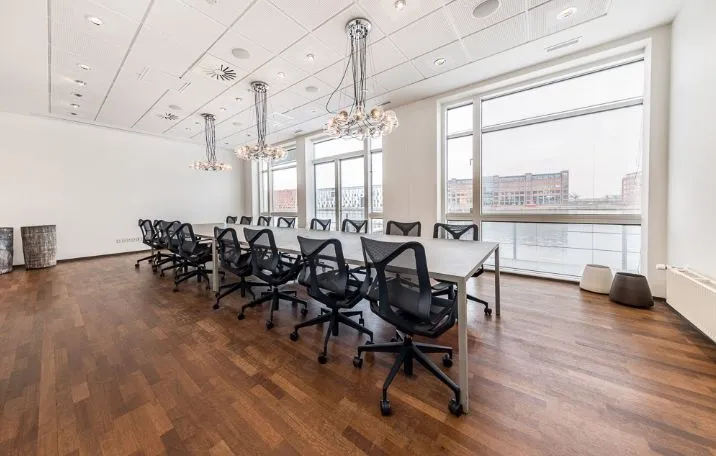 Kontorrum med lysegul gulvbelægning og runde bord med stole og to lysekroner i loftet