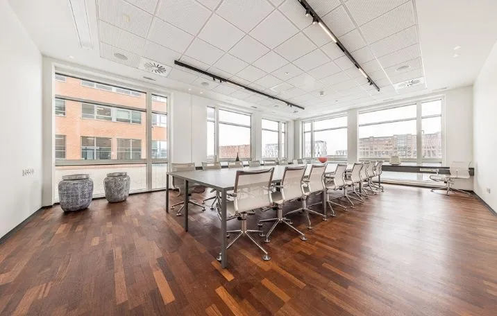 Kontor med store vinduer og trægulv med flere stole og lange borde placeret i stueetagen