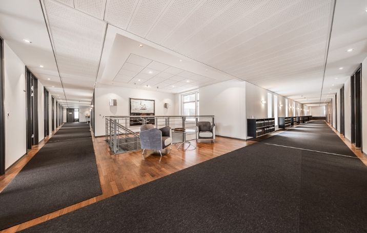 Kontorlokaler med moderne design, højt til loftet, lysegulv, og slanke hjørner. Møblerne er minimalistiske og stilfulde.