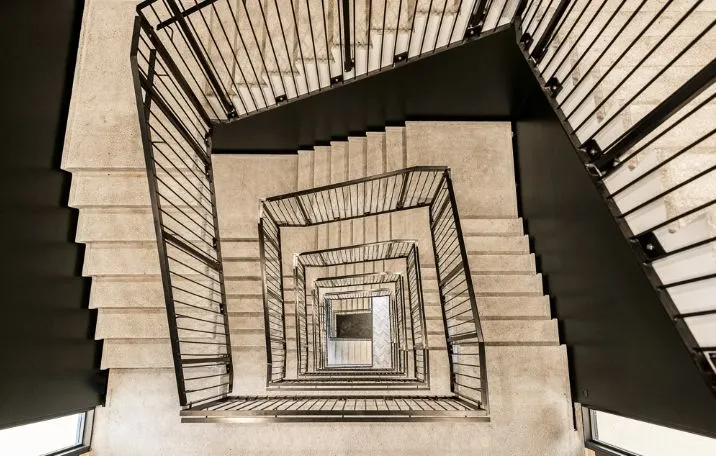 Moderne spiraltrappe i nyopført kontorejendom med sort metal og beige marmortrin. Indbygget lys og gulvbeklædning. Flere