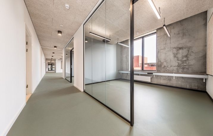 Kontorlokation med store spejlvinduer og grønne gulvbelægning, højloftede lokaler med lyse lofter og moderne indretning
