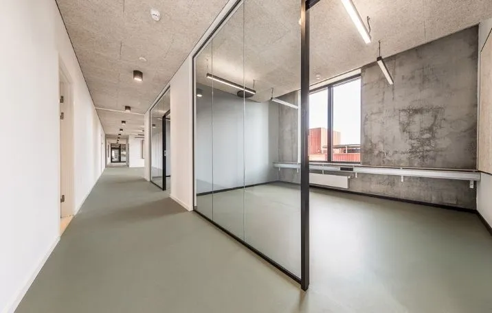 Kontorlokation med store spejlvinduer og grønne gulvbelægning, højloftede lokaler med lyse lofter og moderne indretning