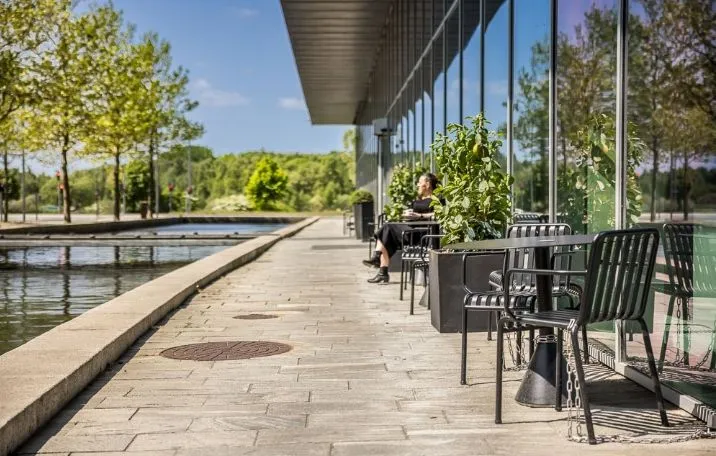 Kvinde sidder på terrasse og nyder udsigten over en kunstig vandkanal med planter og stole i nærheden