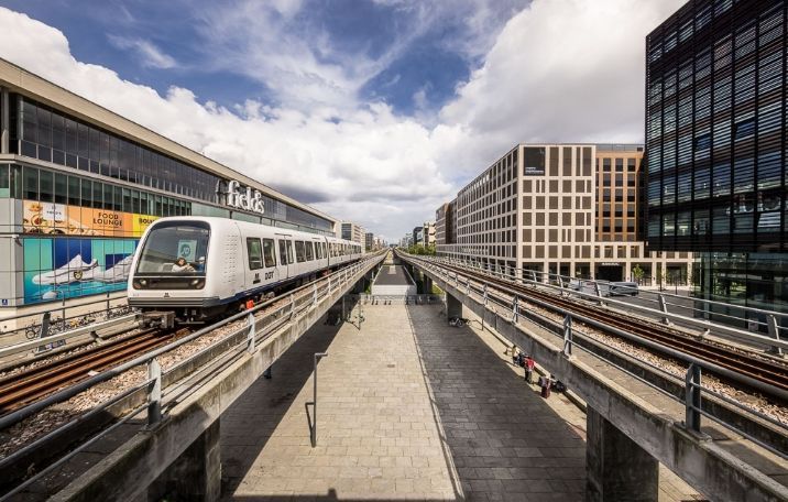 Hvid metro på skinner i en stor by med glasbygninger og skyer i baggrunden
