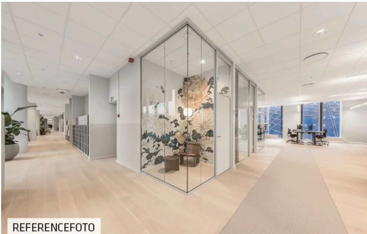 En møbelfri kontorlounge med lyse trægulve og hvide lofter og vægge samt et glasadskillelsesrum med en blomsterdekoration