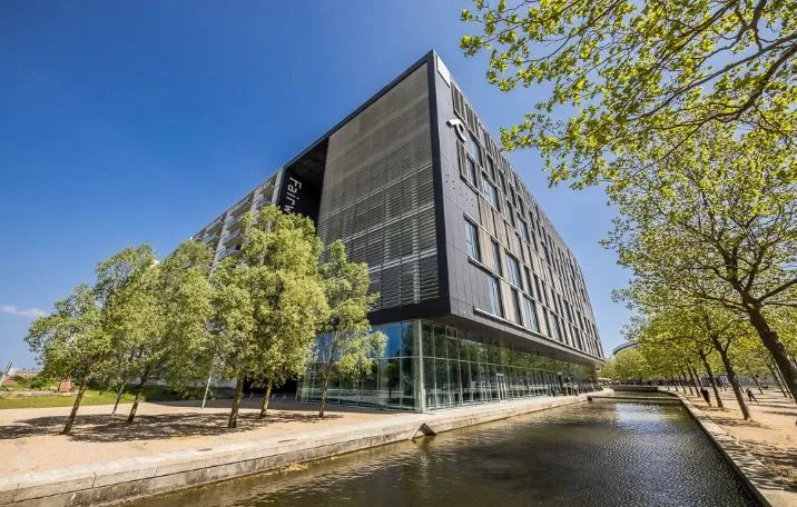 Kontorbyggeri med glasfacade, træer og vandløb langs siderne. Fælles reception og udsigt til Amager Fælled
