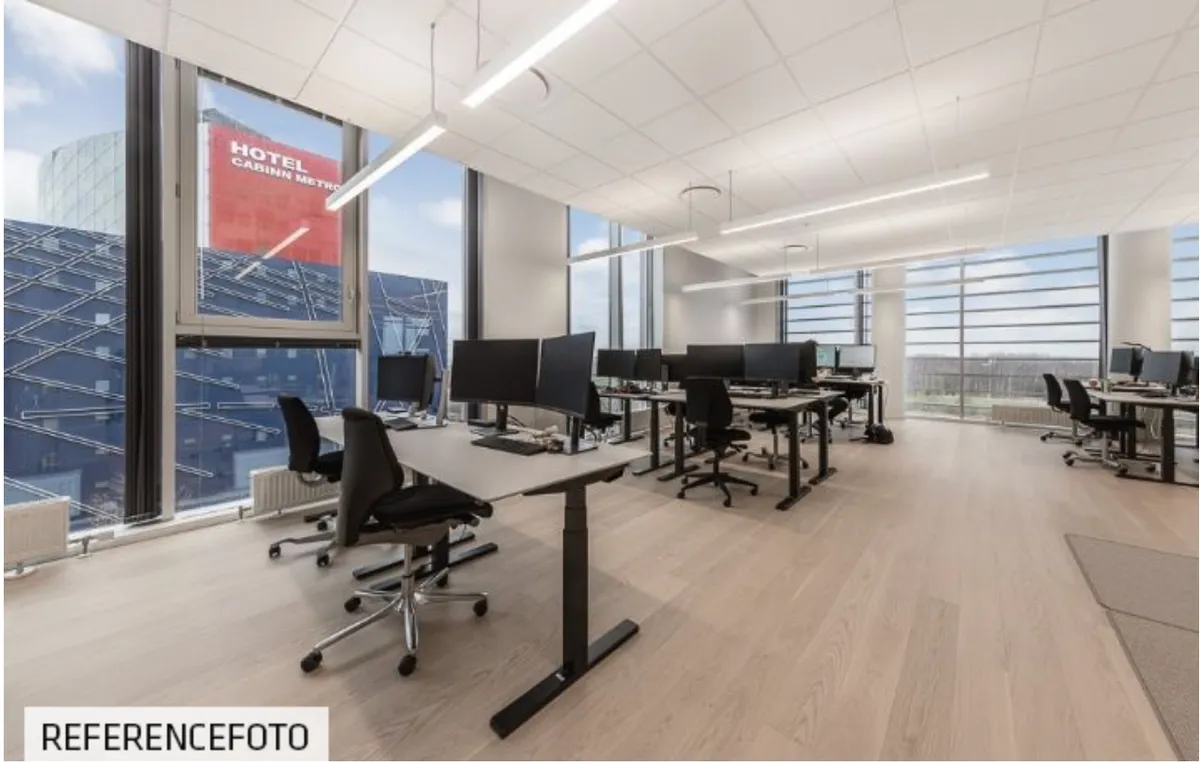 Moderne kontor med lyse lofter, store vinduer, lysegul gulv og ergonomiske skriveborde med skærme og stole