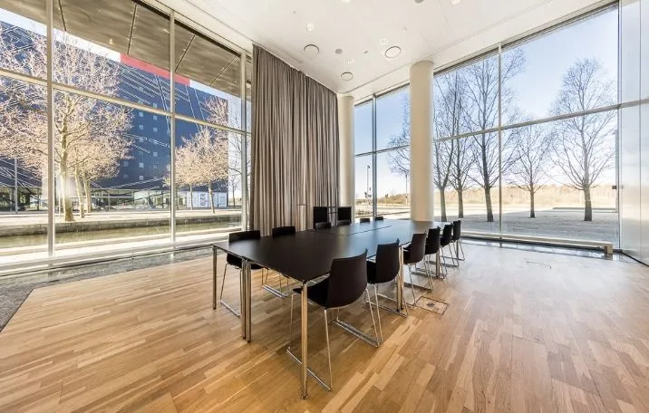 Mødelokale med moderne møbler og store vinduer med udsigt til byen og park.