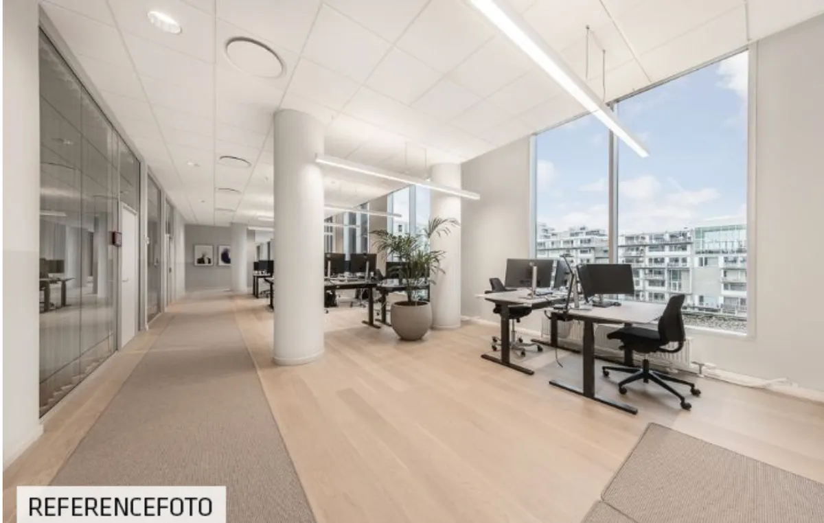 Moderne kontor med lyse lofter og glasvinduer, udstyret med skriveborde, computere og potteplanter, beliggende med udsigt