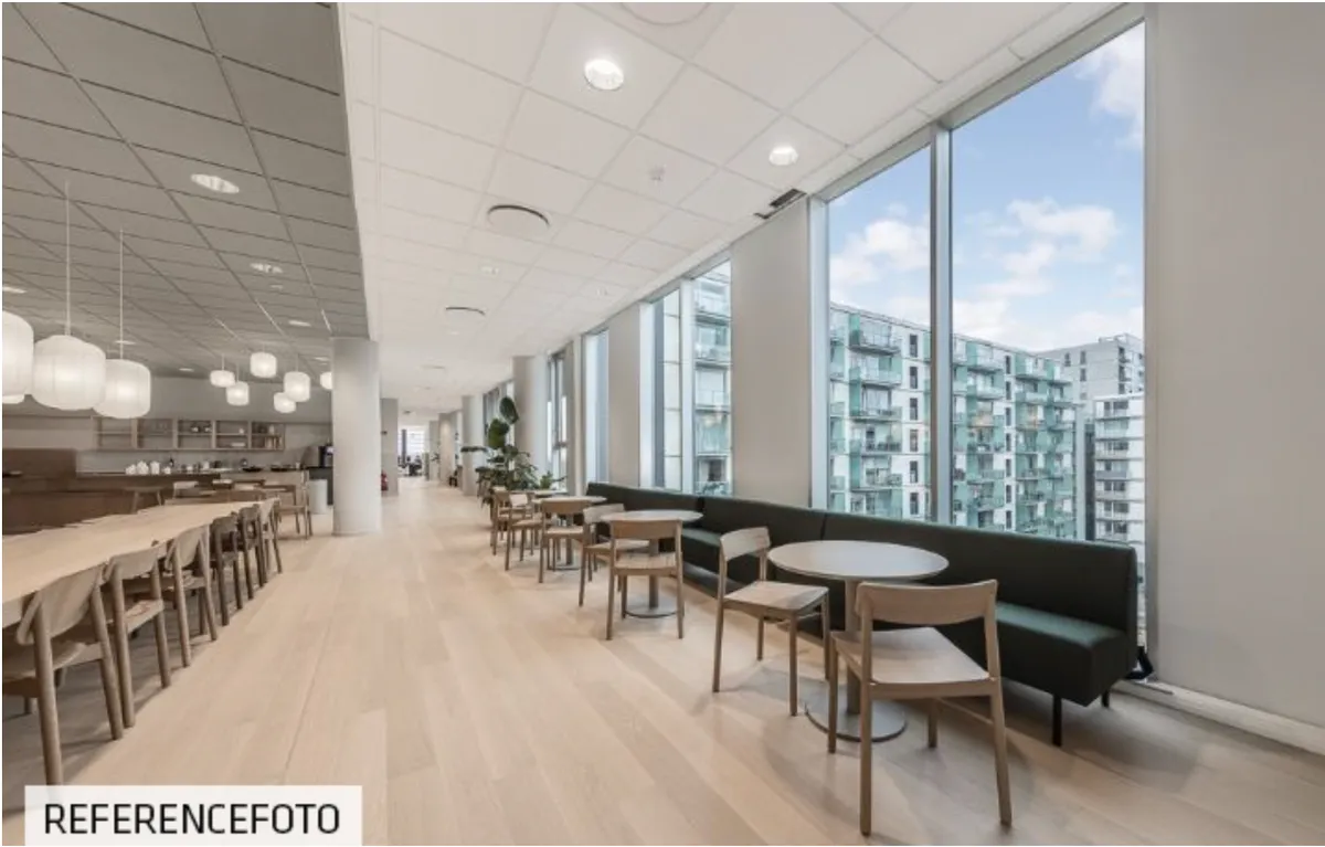 Moderne kontor med lyse lofter og store vinduer med udsigt til bygninger og grønne områder